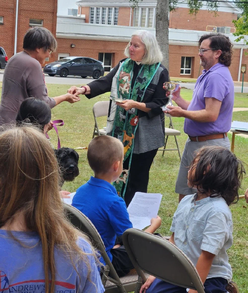 Communion at the outdoor Mass on the Grass service, with a black dog seated among the congregation