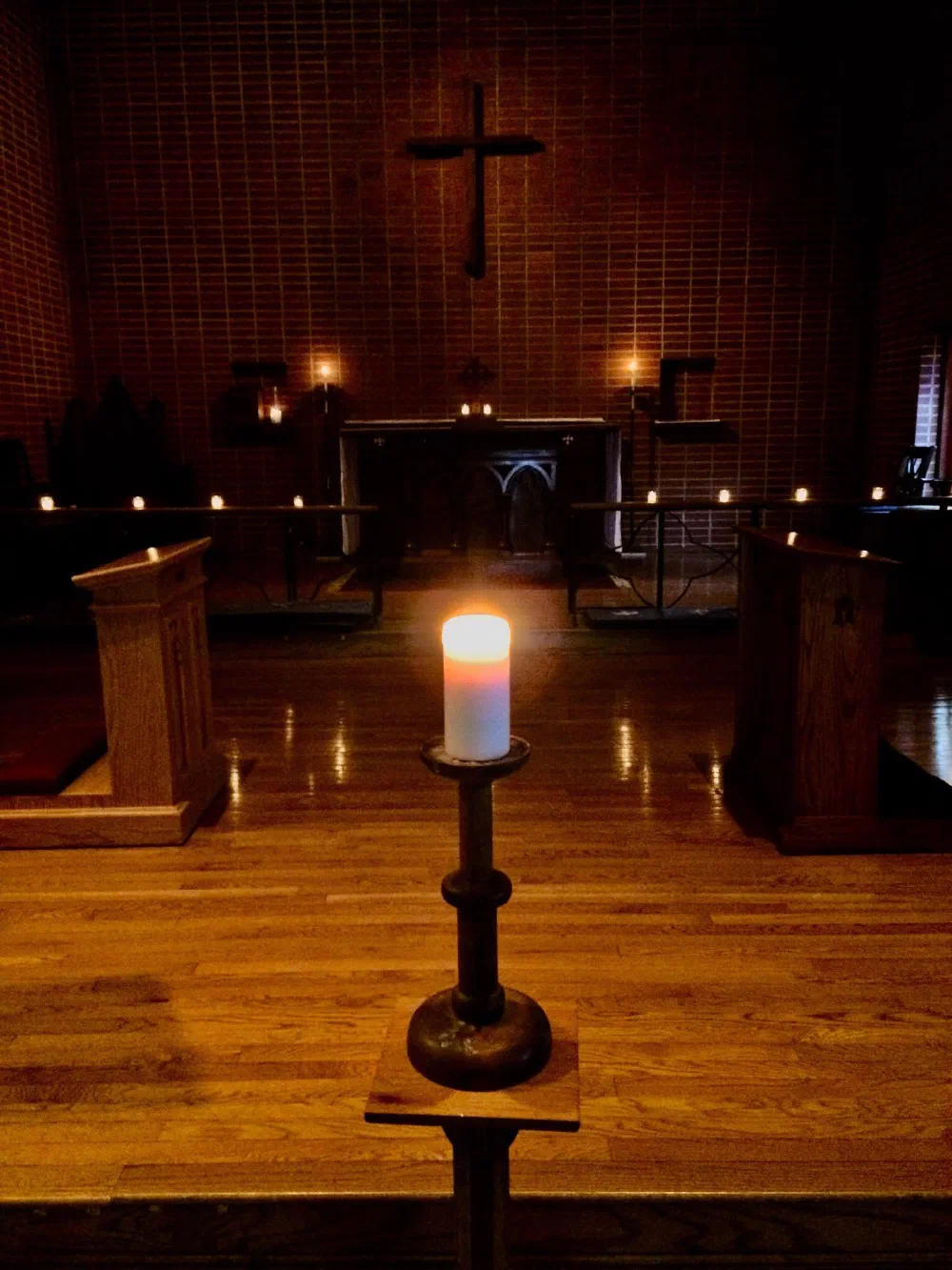 The darkened chancel lit by a single tall candle, with small candles glowing along the altar rail
