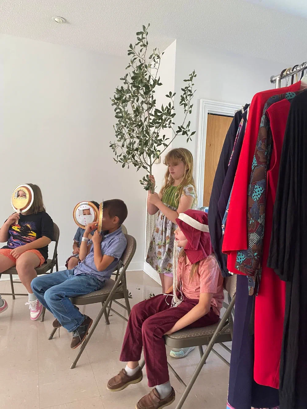 A child lifts an olive branch while others hold handmade masks during Children's Chapel drama time