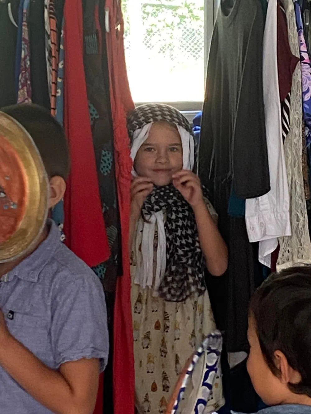 A smiling child in a headscarf costume stands among the dress-up clothes during Children's Chapel