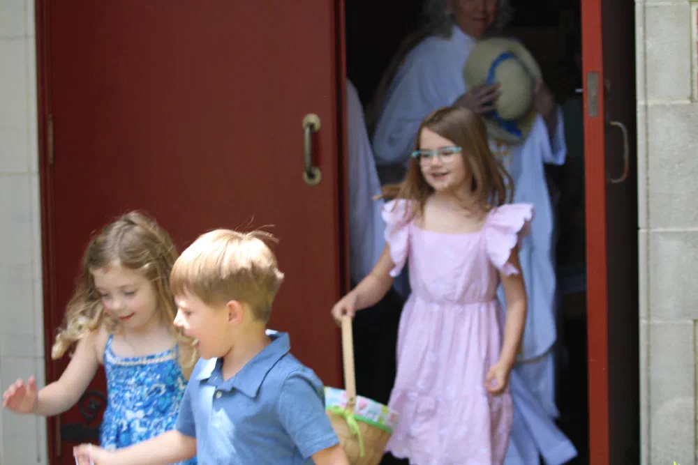 Children with Easter baskets burst out of the red church doors into the sunlight