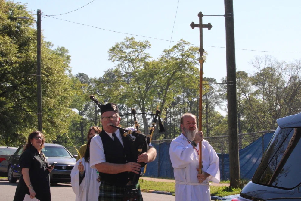A bagpiper in a kilt leads the Palm Sunday procession beside a crucifer carrying the processional cross
