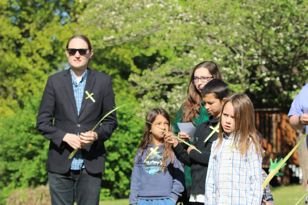 Families and children holding palm fronds and wearing palm crosses outdoors on Palm Sunday