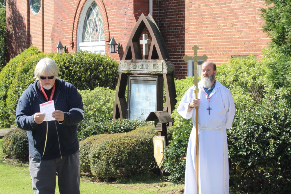 A reader and a crucifer in a white alb with the processional cross pause outside a neighboring church during the Palm Sunday procession