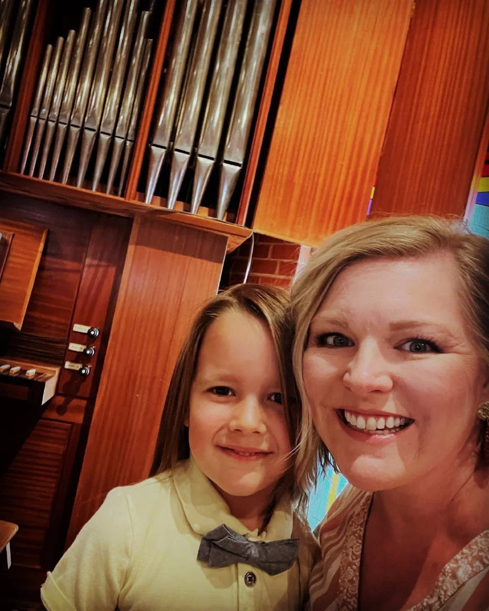 A smiling musician and a boy in a bow tie take a selfie in front of the pipe organ