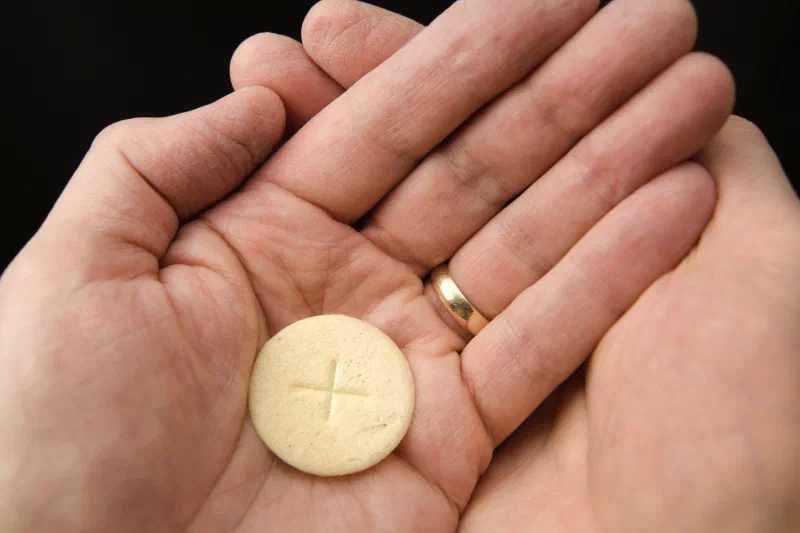 A communion wafer marked with a cross, held in open hands